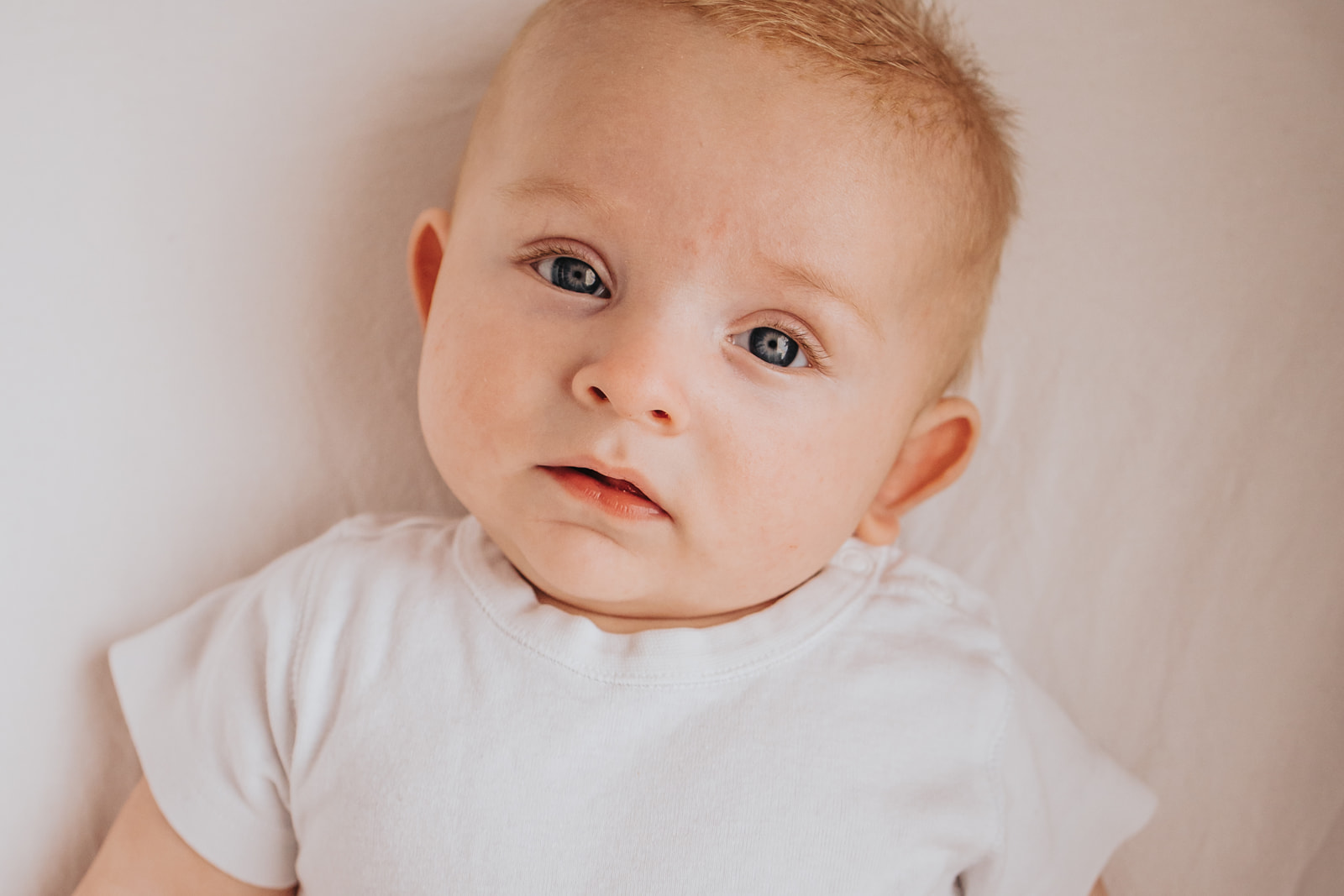 bebisporträtt med vit tröja tittar in i kameran