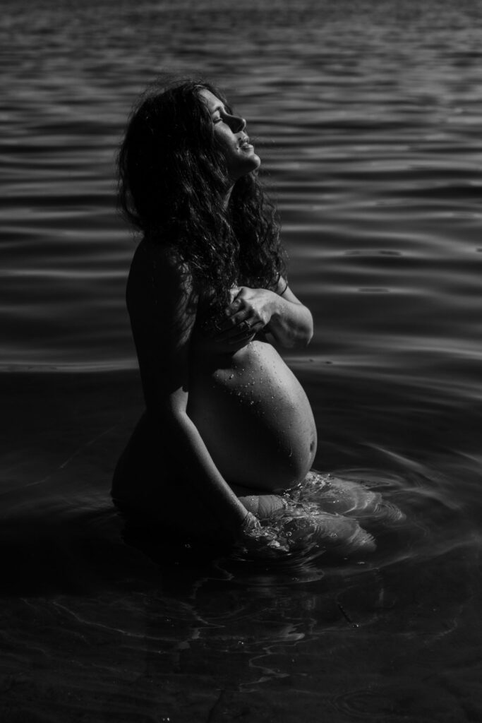 gravid kvinna som sitter naken i vattnet och njuter av solen
