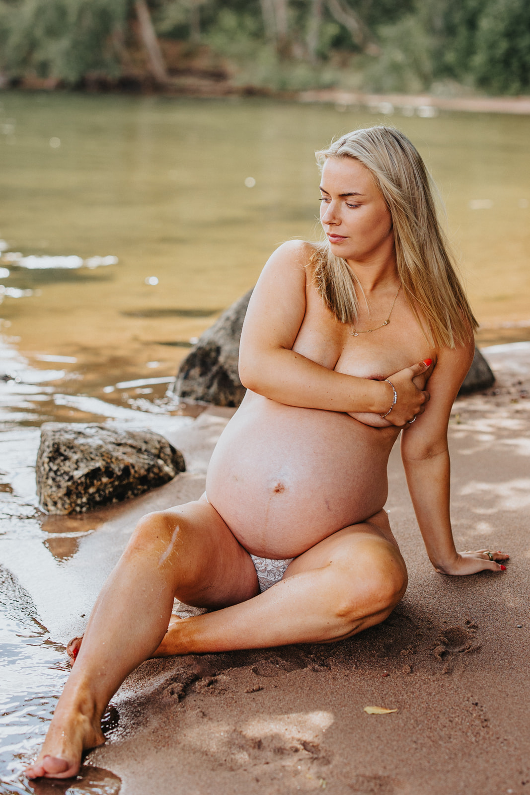 gravid kvinna sitter på stranden intill vattnet och skyler sig