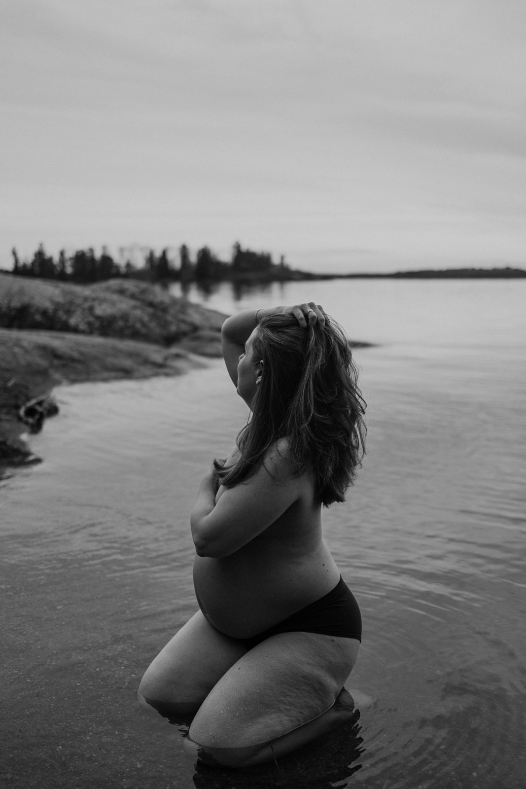 gravid kvinna sitter med underkläder i vattnet och kollar bortåt