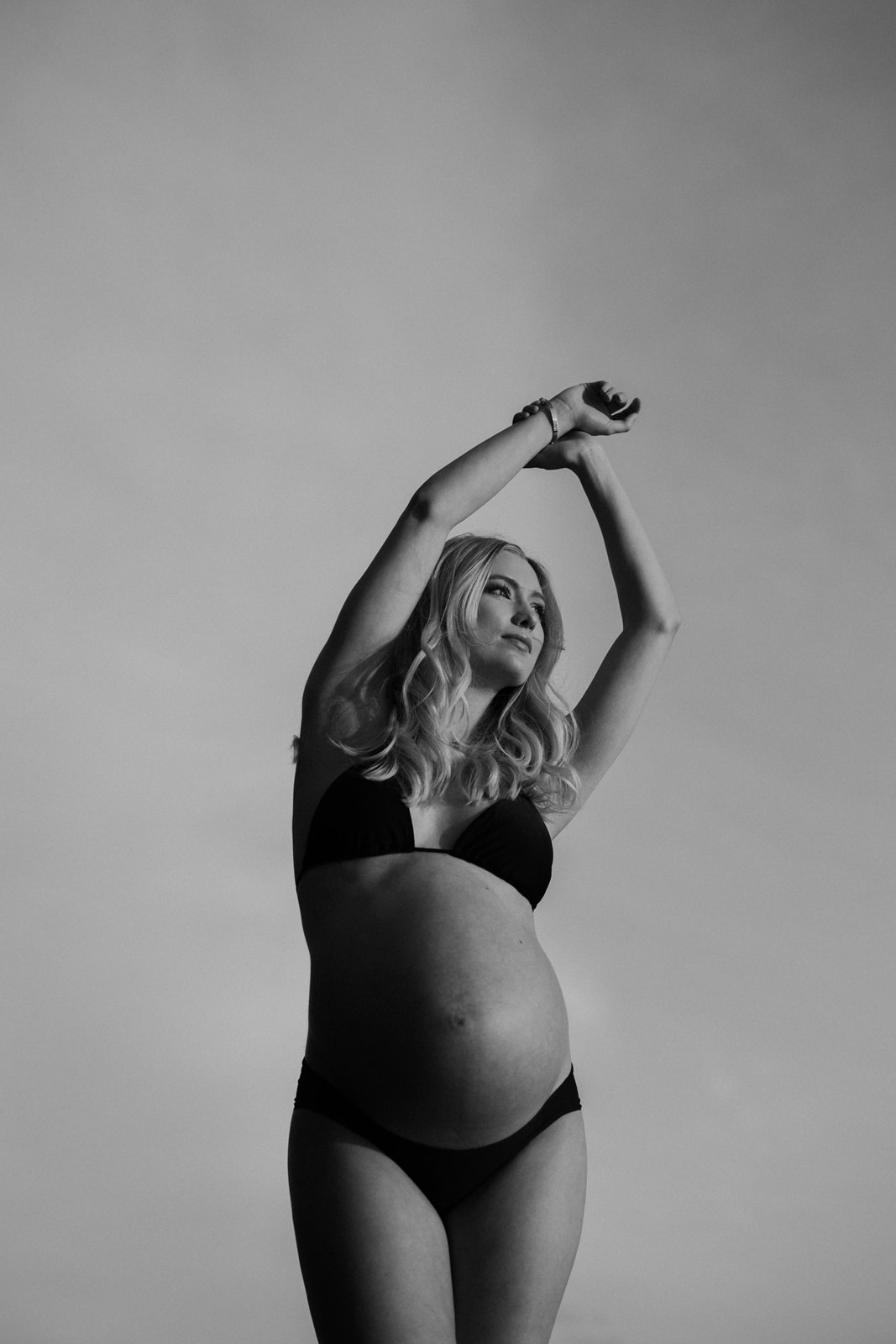 gravid kvinna står i svart bikini med armarna över huvudet