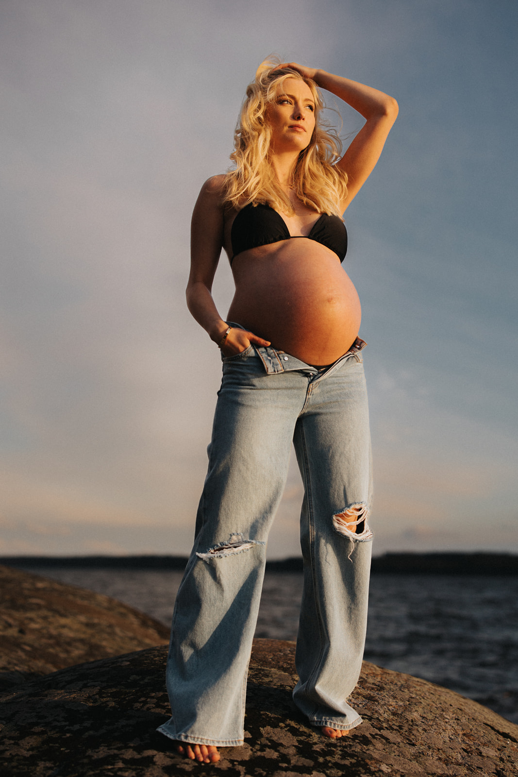 gravid kvinna står i jeans och svart bikini på ett berg
