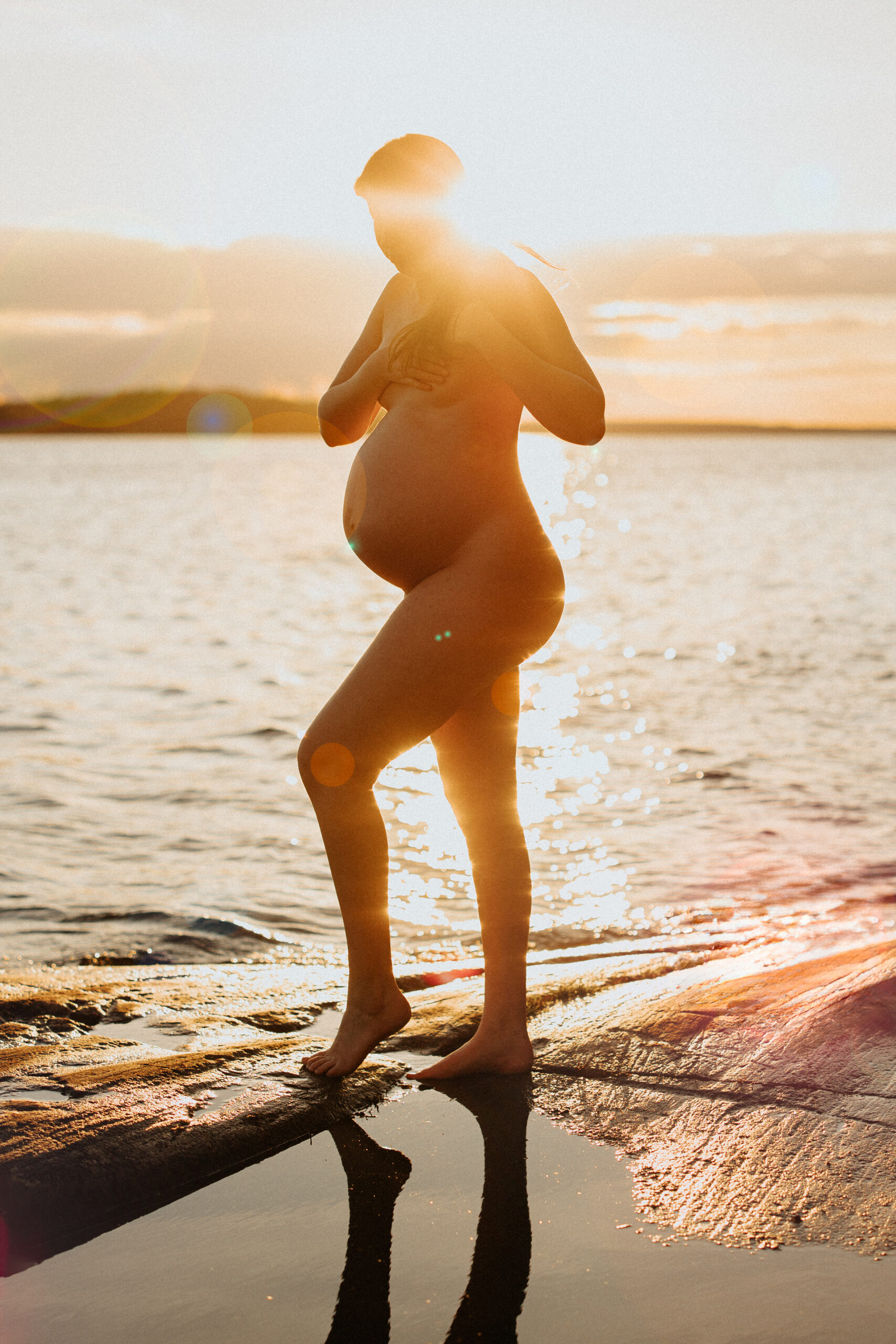 gravid kvinna står i solnedgången vid vattnet
